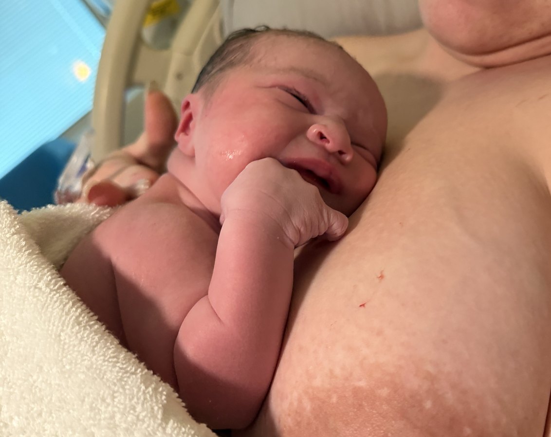 Newborn baby resting skin to skin on their mother’s chest, one tiny hand curled near their cheek